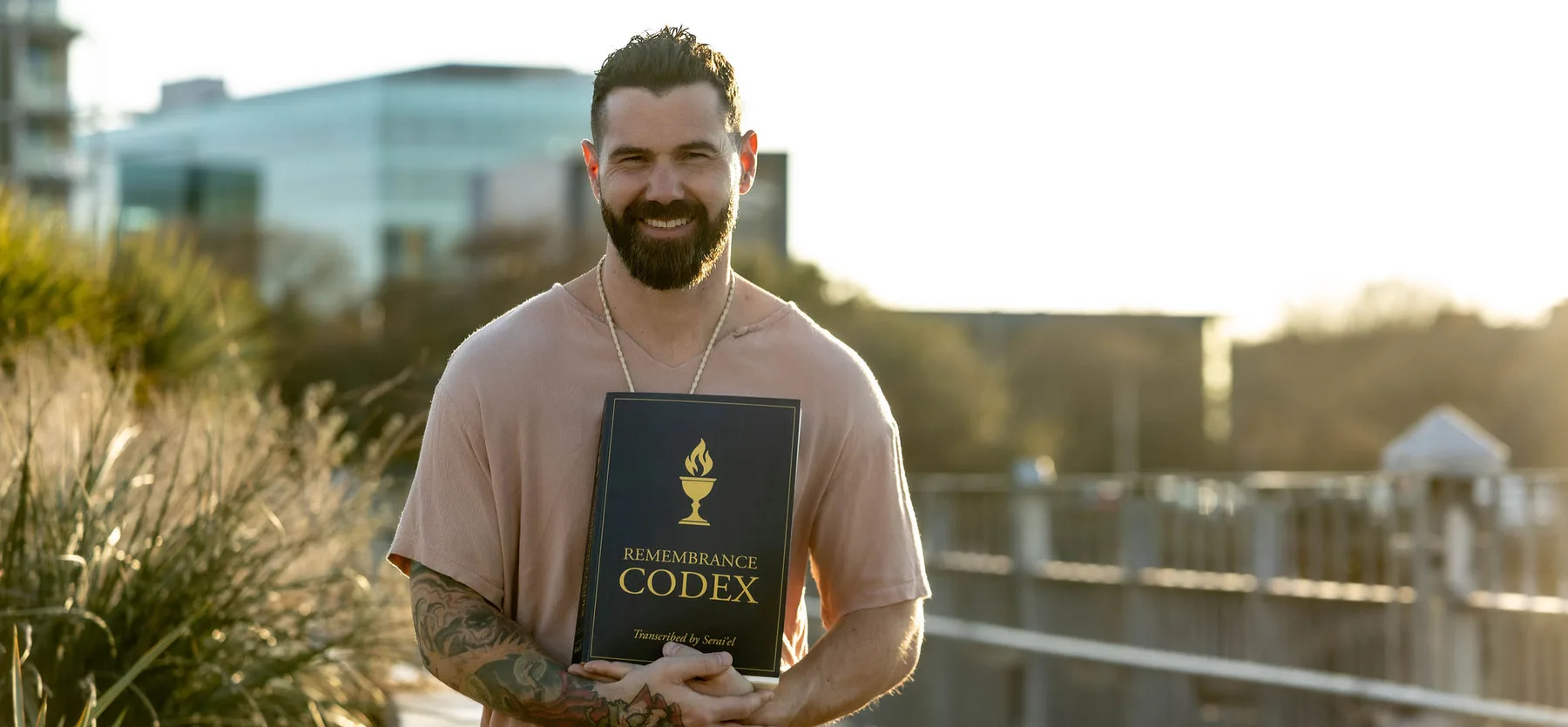 Zack Blakeney holding the Remembrance Codex volume on a boardwalk at sunset.